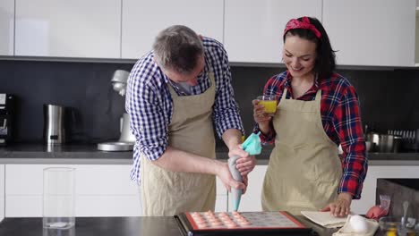 Man-Piping-Out-Macaron-Mixture-On-A-Slip-Mat-With-Watching-His-Wife