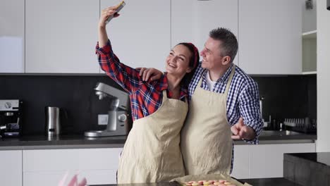 Glückliches-Ehepaar-In-Schürzen-Macht-Ein-Selfie-In-Der-Küche
