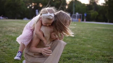 Happy-Mom-With-Long-Blonde-Hair-Laughing-While-Piggybacking-Her-Little-Little-Girl-Through-A-Green-Park-In-Slow-Motion