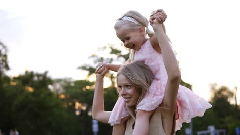 Glückliche-Mutter-Trägt-Schöne-Kleine-Tochter-Auf-Ihren-Schultern,-Tanzt-Und-Hat-Gemeinsam-Spaß-Im-öffentlichen,-Grünen-Park