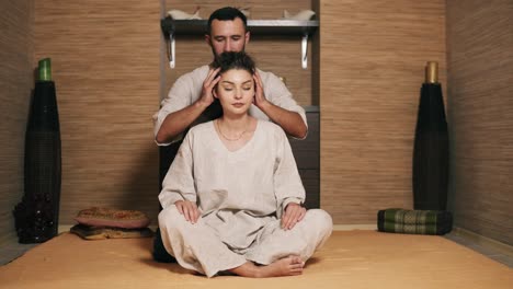 Der-Attraktive-Thai-Massager-Massiert-Den-Kopf-Der-Jungen-Frau,-Die-Hinter-Ihr-Sitzt