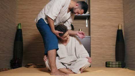 Male-Thai-Massagist-Is-Massaging-Young-Woman's-Neck-With-His-Elbow-Standing-Nearby-Her