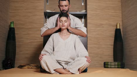 Attractive-Thai-Massagist-Is-Massaging-Young-Woman's-Head-Sitting-Behind-Her-2