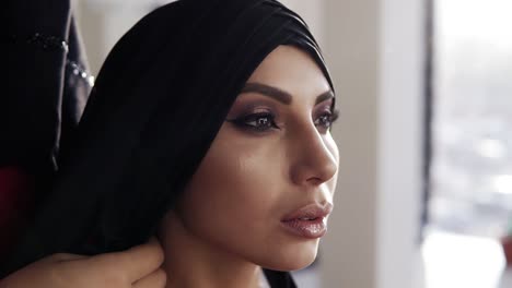 Schönes-Mädchen-Mit-Traditionellem-Arabischem-Schwarzem-Hijab,-Das-Ihren-Kopf-Von-Einer-Nicht-Erkennbaren-Frau-Hinter-Ihrem-Rücken-Bedeckt