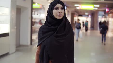 Portrait-Of-A-Stylish-Young-Muslim-Woman-In-Black-Hijab-And-Tight-Brown-Dress-With-Bags-In-Her-Hands-After-Shopping-Walking-By-Shopping-Mall-1