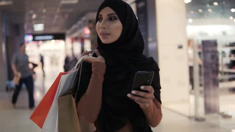 Attractive-Muslim-Woman-Wearing-Black-Hijab-Headscarf-Walking-In-The-Shopping-Mall-And-Using-Smartphone