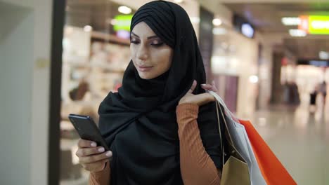 Attractive-Muslim-Woman-Wearing-Black-Hijab-Headscarf-Walking-In-The-Shopping-Mall-And-Using-Smartphone-1