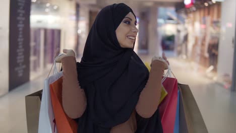 Mujer-Musulmana-Bastante-Joven-Con-Maquillaje-Perfecto-Sosteniendo-Varias-Bolsas-De-Compras-Coloridas-Después-De-Comprar-Y-Sonriendo-A-La-Cámara