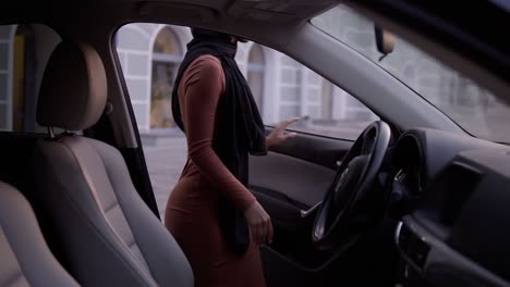 Young-Beautiful-Muslim-Girl-In-Black-Hijab-Open-The-Door-And-Sitting-In-Car,-Watching-At-Mirror,-Fixing-It