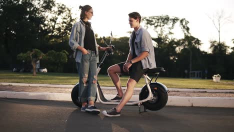 Young-Beauty-Boy-And-Girl-Outside-Near-The-Bike-On-The-Road,-The-Young-Female-Is-Sitting-On-Bike-And-Flirting-To-The-Girl
