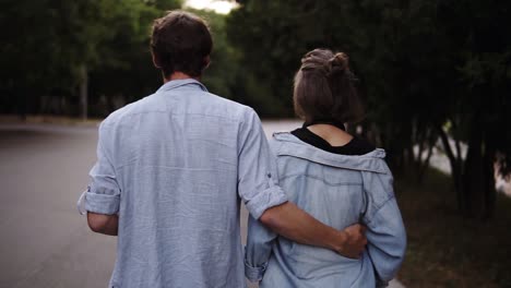 Traking-Footage-Of-A-Young-Couple-Both-In-Blue-Similar-Shirts-Are-Walking-Bonding-By-Park