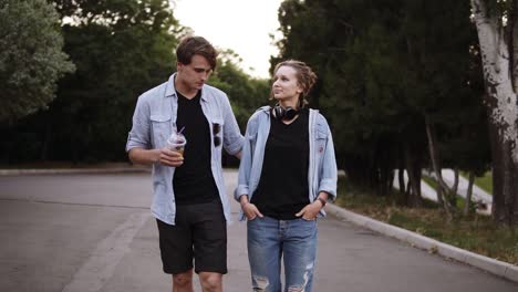 Beautiful-Young-Friends-Both-In-Black-T-Shirts-And-Blue-Shirts-Are-Walking-By-Park-In-The-Evening-Dusk