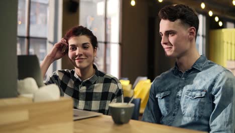Young-Couple-In-Stylish-Hipster-Urban-Outfits-Sitting-In-An-Open-Co-Working-Space,-Discussing-Something-While-Pointing-At-Laptop-Screen