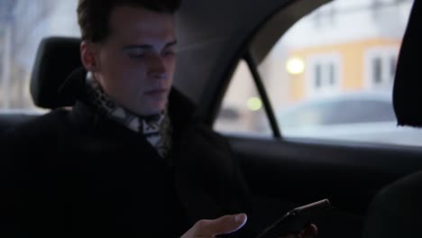 Young-Attractive-Male-Holding-And-Scrolling-Smartphone-While-Sitting,-Riding-In-A-Car