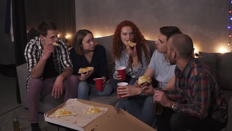 Cheerful-Men-And-Women-Are-Eating-Cheesy-Pizza,-Chatting-Relaxing-During-Indoor-Party-In-Apartment-In-A-Loft-Room