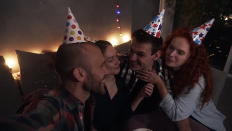 Young-Happy-Friends-Or-Two-Couples-Having-Small,-Cozy-Birthday-Celebration,-Sitting-Together-In-Festive-Cones-And-Taking-Selfie-Or-Looking-To-The-Camera
