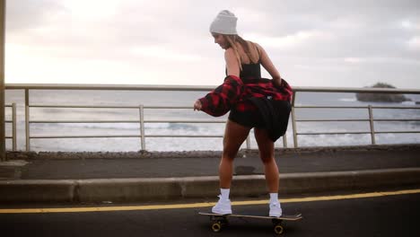 Muscular,-Pretty-Hipster-Woman-In-Plaid-Coat-Having-Fun-Riding-Skateboard-Longboard-Downhill-On-Beautiful-Road-In-Slow-Motion