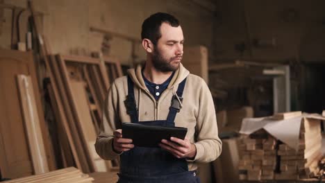 A-Young-Man-With-A-Beard-Walks-Around-The-Carpentry-Shop-With-A-Tablet-In-His-Hands