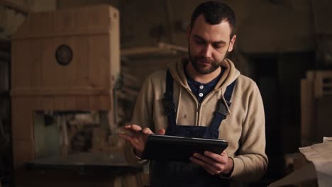 Young-Carpenter-Walking-Through-The-Workshop-With-Tablet-In-Hands