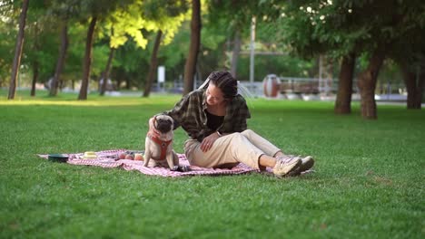 Girl-Sitting-On-Plaid-On-Lawn-In-A-Park-While-Dog-Sitting-In-Front-Of-Her,-She-Pets-Him