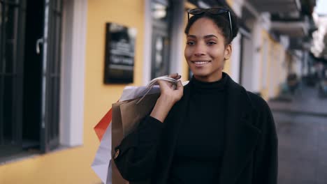 Portrait-Of-An-Attractive-Mixed-Race-Girl-Smiling-While-Walking-Down-The-Street-With-Colorful-Shopping-Bags