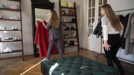 Long-Haired-Young-Blonde-Female-Is-Trying-A-New-Grey-And-Red-Coats-While-Standing-In-Front-The-Mirror