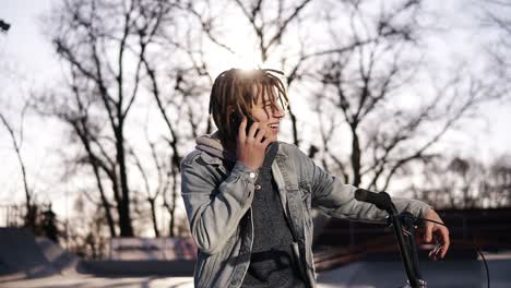 Portrait-Of-Happy-Handsome-Teenage-Boy-With-Dreadlocks,-Using-Mobile-Phone-While-Riding-A-Bmx-Bike,-Smiling,-Messaging-Friends-Via-Social-Networks
