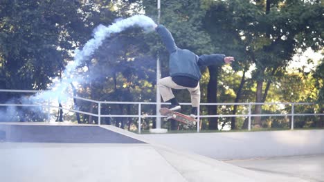 Young-Guy-Practicing-On-Sunny-Summer-Day-While-Holding-Blue-Coloured-Burning-Smoke-Bomb-On-The-Skate-Ramp