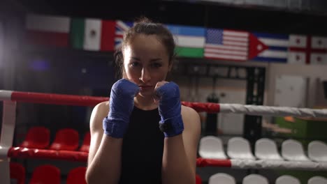 Close-Up-Shot-Of-Confident-Female-Fighter-With-Wrapped-Hands-Looking-At-Camera-While-Posing-In-Gym