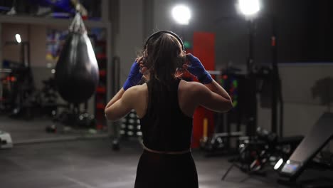 Fit-Female-Boxer-Walks-By-Boxing-Gym-In-Headphones,-Warming-Up
