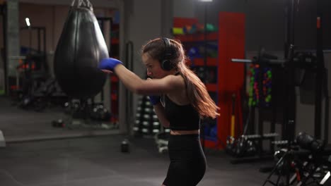 Female-Boxer-Performing-Active-Punching-In-Bandages,-Wearing-Headphones