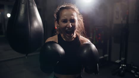 Portrait-Of-Female-Boxer-Standing-At-Dark-Gym,-Looking-Intensely-At-The-Camera-And-Screaming