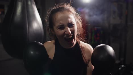 Female-Boxer-Standing-At-Dark-Gym,-Looking-Intensely-At-The-Camera-And-Screaming