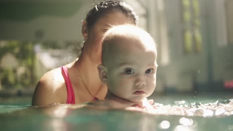 Feliz-Madre-Y-Su-Bebé-Están-Nadando-En-La-Piscina-Cubierta,-Agitándolo-Bajo-El-Agua