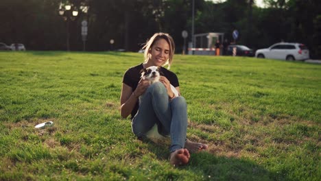 Beautiful-Young-Woman-In-Casual-Sitting-On-Grass-With-Her-Dog-Pet-And-Smiling