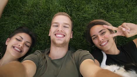 Drei-Attraktive-Tausendjährige-Freunde-Machen-Selfies,-Während-Sie-Auf-Dem-Grünen-Gras-Im-Park-Oder-Auf-Dem-Rasen-Liegen