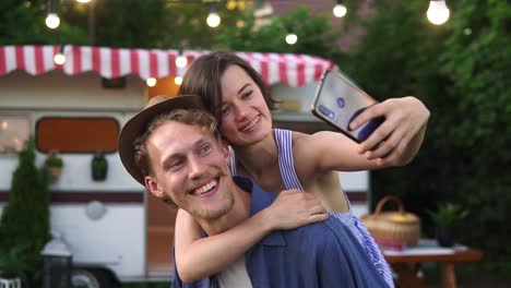 Happy-Young-Lovely-Couple-Having-Fun-Near-Trailer-In-The-Park,-Man-Piggybacking-Girl-1