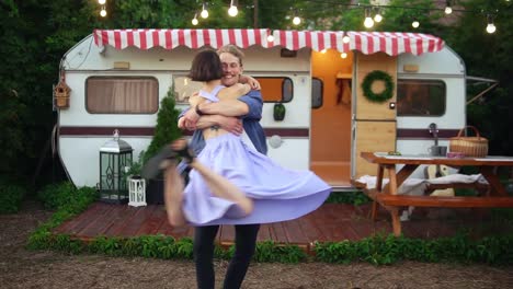 Lovely-Couple-Having-Fun-Near-Trailer-In-The-Park,-Slender-Girl-Jumping-Into-Arms-Ofher-Boyfriend-And-Spinning-Her-Around