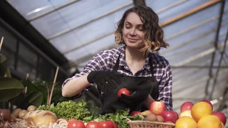 Low-Angle-View-Of-A-Beautiful,-Smiling-Woman-Farmer-In-Black-Gloves-Arranging-Organic-Food-In-Farm-Market-Standing-Indoors-In-Spacious-Greenhouse