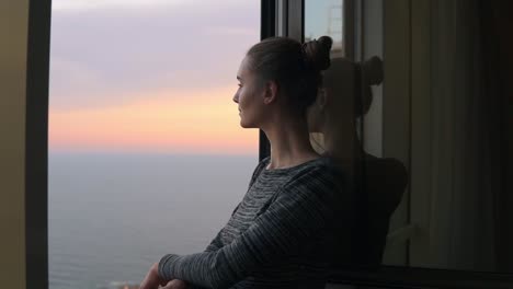 Closeup-View-Of-Beautiful-Young-Woman-Standing-By-The-Open-Window-During-The-Sunset-By-The-Sea-And-Enjoying-The-View