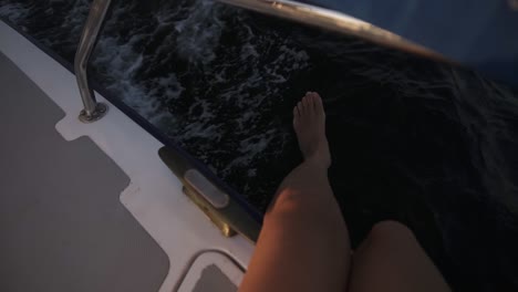 Top-View-Of-A-Nice-Women's-Legs-Playfully-Hanging-Above-Sea-From-Yacht-On-Sunlight-In-Slow-Motion