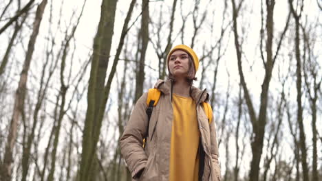 A-Young-Girl-In-A-Yellow-Wool-Cap-In-The-Forest-Looks-Up-At-The-High-Branches-Of-The-Trees-1