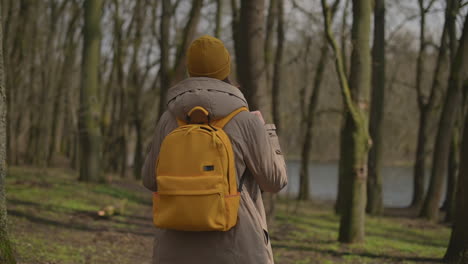 A-Young-Girl-In-A-Yellow-Wool-Cap-And-A-Yellow-Backpack-Walks-Through-The-Forest-Looking-From-Side-To-Side