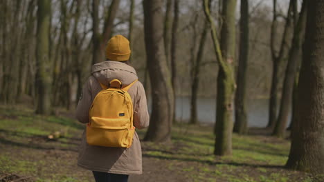 A-Young-Girl-In-A-Yellow-Wool-Cap-And-A-Yellow-Backpack-Walks-Through-The-Forest-Looking-From-Side-To-Side-1