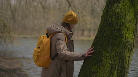 A-Young-Girl-In-A-Yellow-Wool-Cap-And-A-Yellow-Backpack-Walks-Through-The-Forest-Towards-The-Lake-1