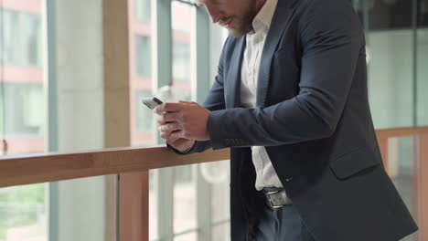 An-Attractive-Young,-Bearded-Businessman-In-A-Blue-Blazer-Consults-His-Smart-Phone-Attentively