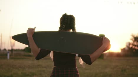Back-View-Of-Woman-In-Plaid-Shirt-And-Tank-Top-Holding-Longboard-And-Walking-During-The-Sunset-In-Summertime