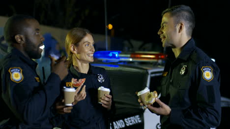 Mixed-Races-Male-And-Female-Police-Officers-Talking-Cheerfully-And-Having-Break-At-Patrolling-On-Street-At-Night