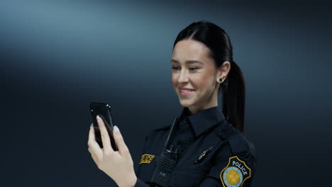 Young-Joyful-Pretty-Policewoman-In-Uniform-Smiling-And-Having-Videochat-On-The-Smartphone-Via-Web-Cam-On-The-Dark-Wall-Background