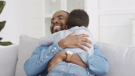 Happy-Cheerful-Man-Hugging-His-Small-Cute-Son-And-Laughing-At-Home-On-Couch-1